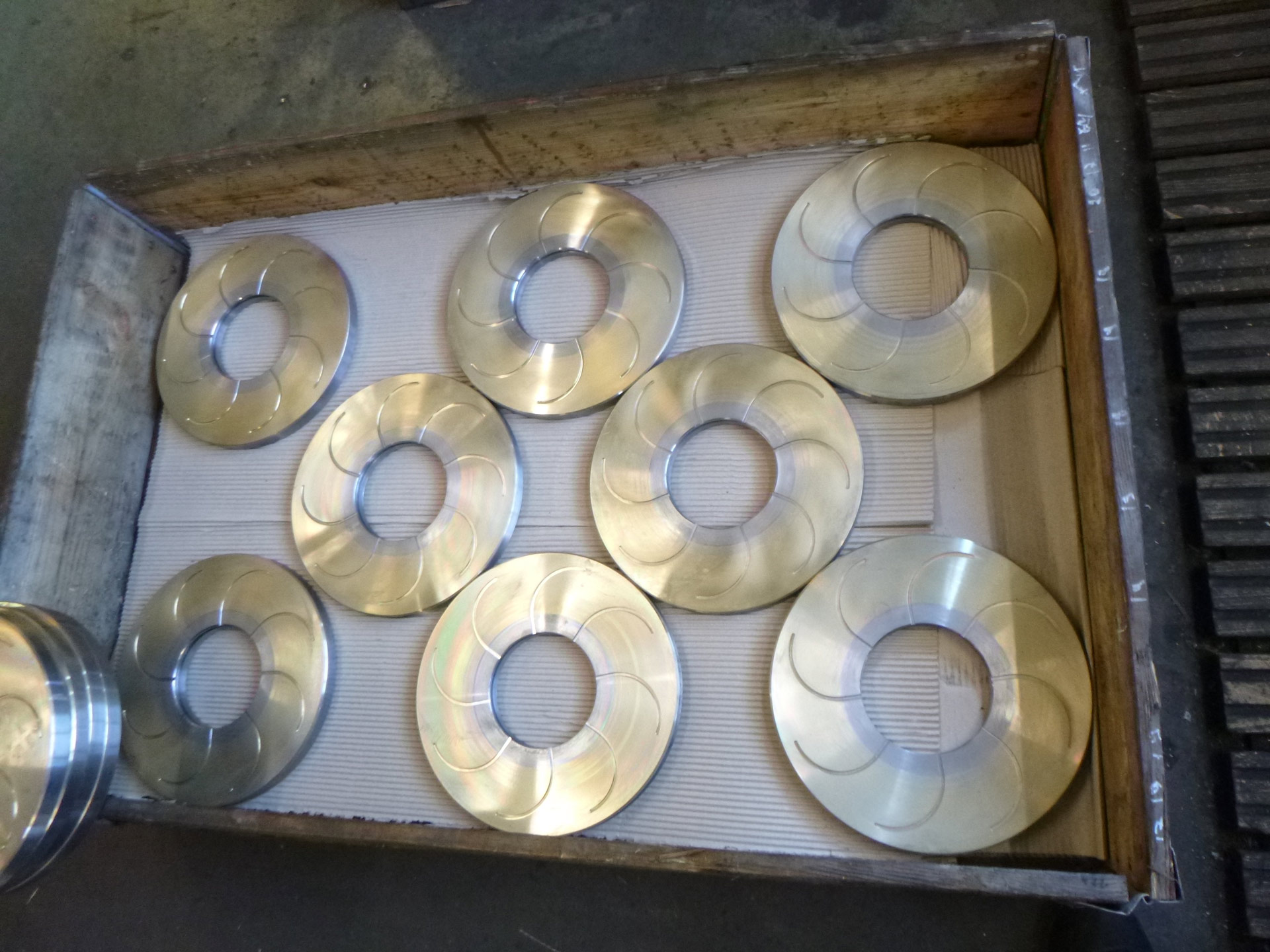 Kiste mit acht glänzenden Metallscheiben auf Wellpappe in warmem Licht.