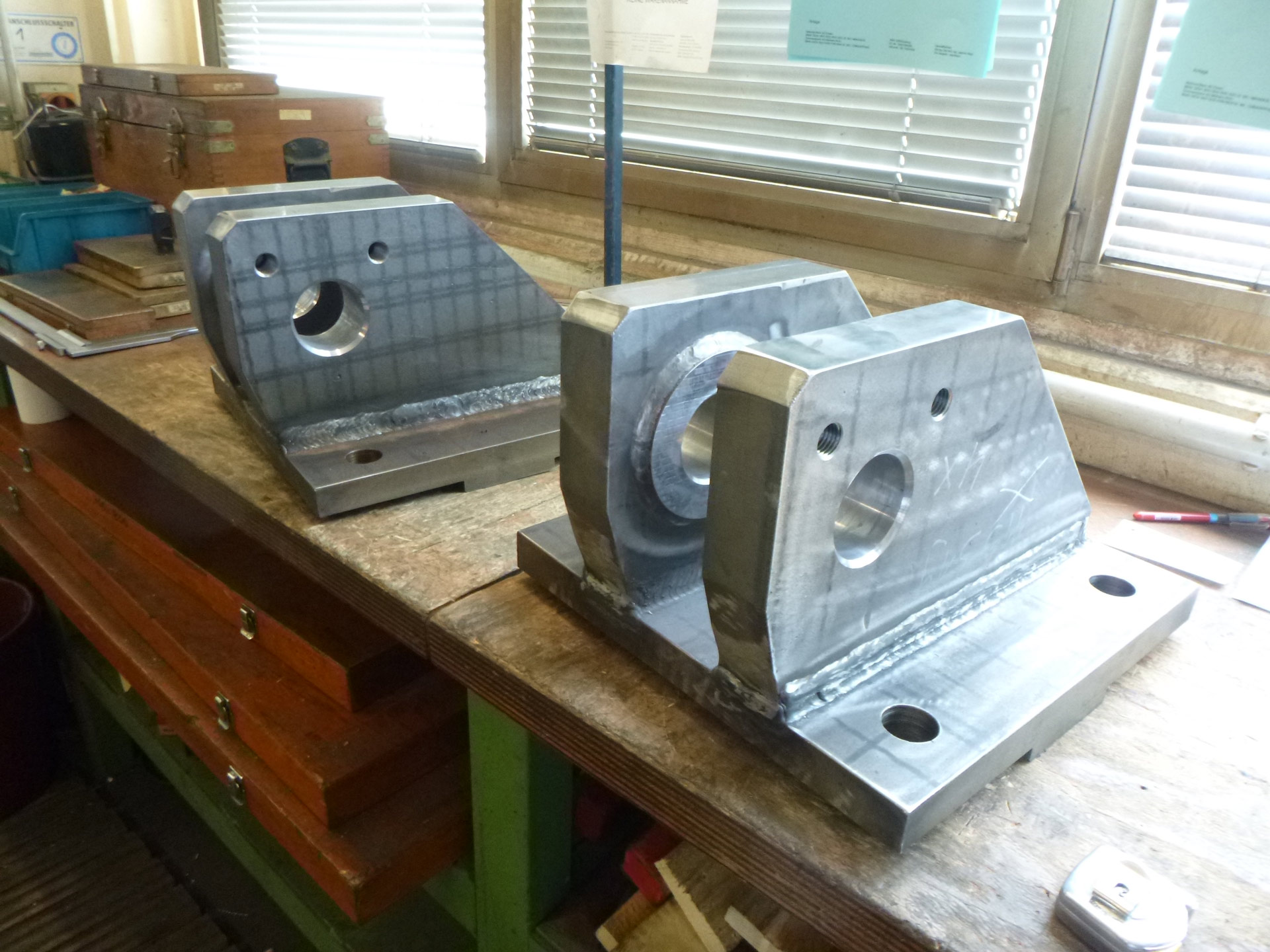 Zwei bearbeitete Metallteile auf einer Werkbank in einem Werkstattumfeld.