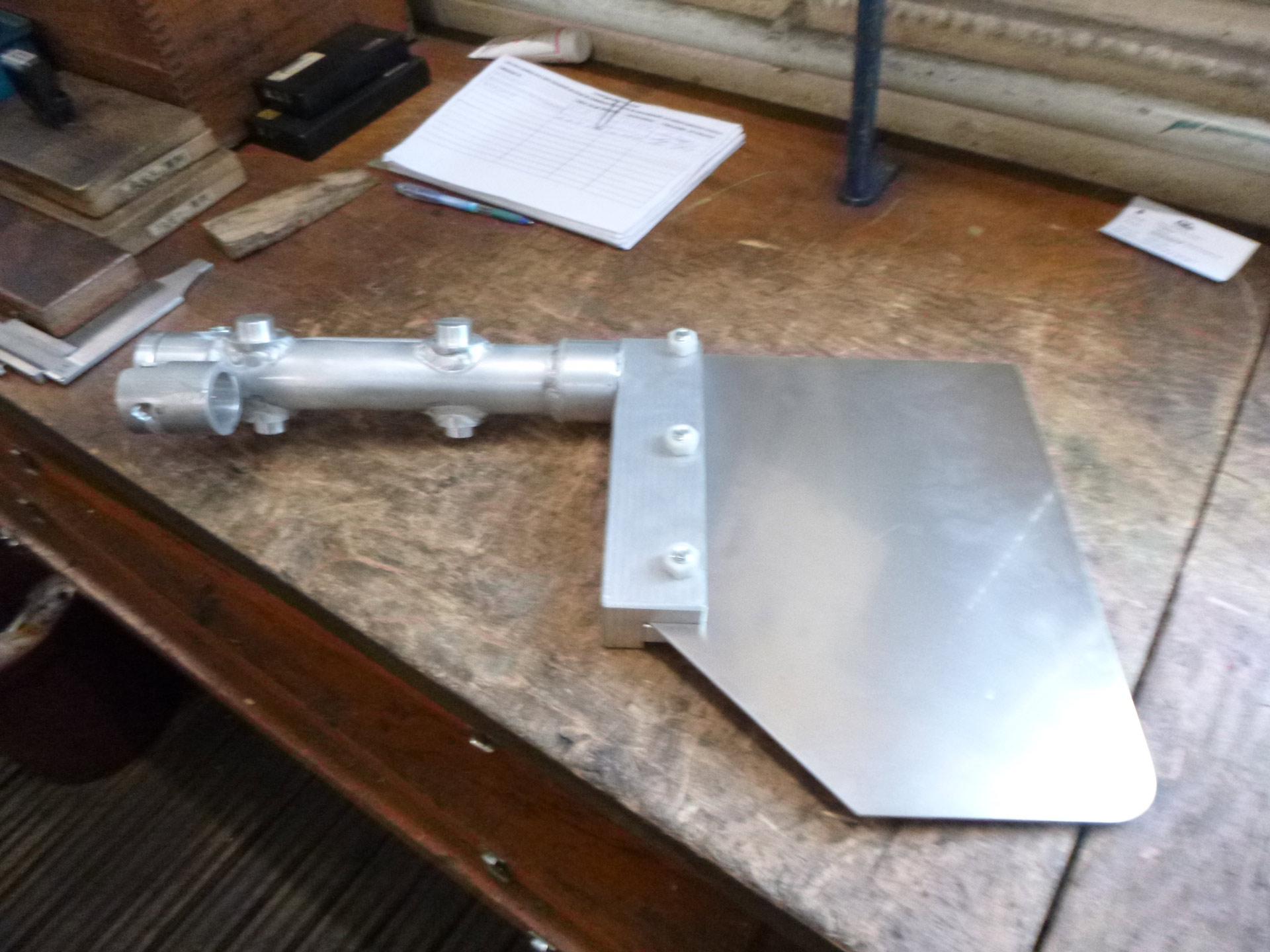 Metallisches Gerät auf einem Holztisch mit Papieren im Hintergrund.